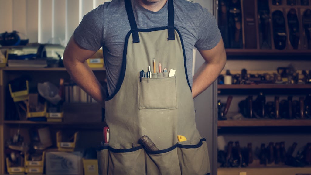 Close-up of a craftsperson with tools in an apron, engaging in work.