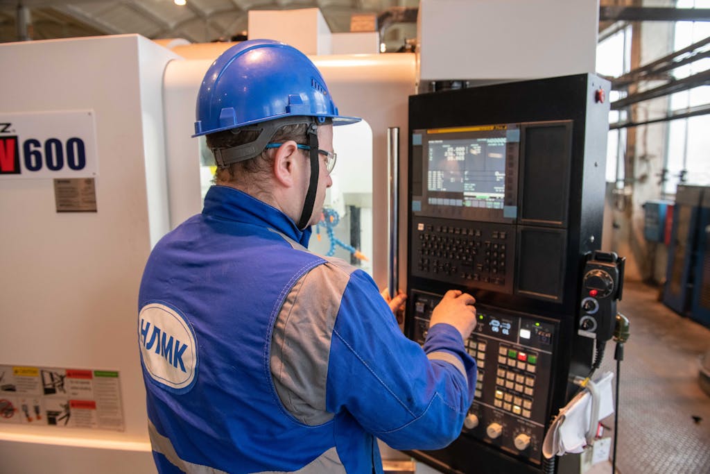Russian factory worker in blue uniform operating CNC machine indoors.