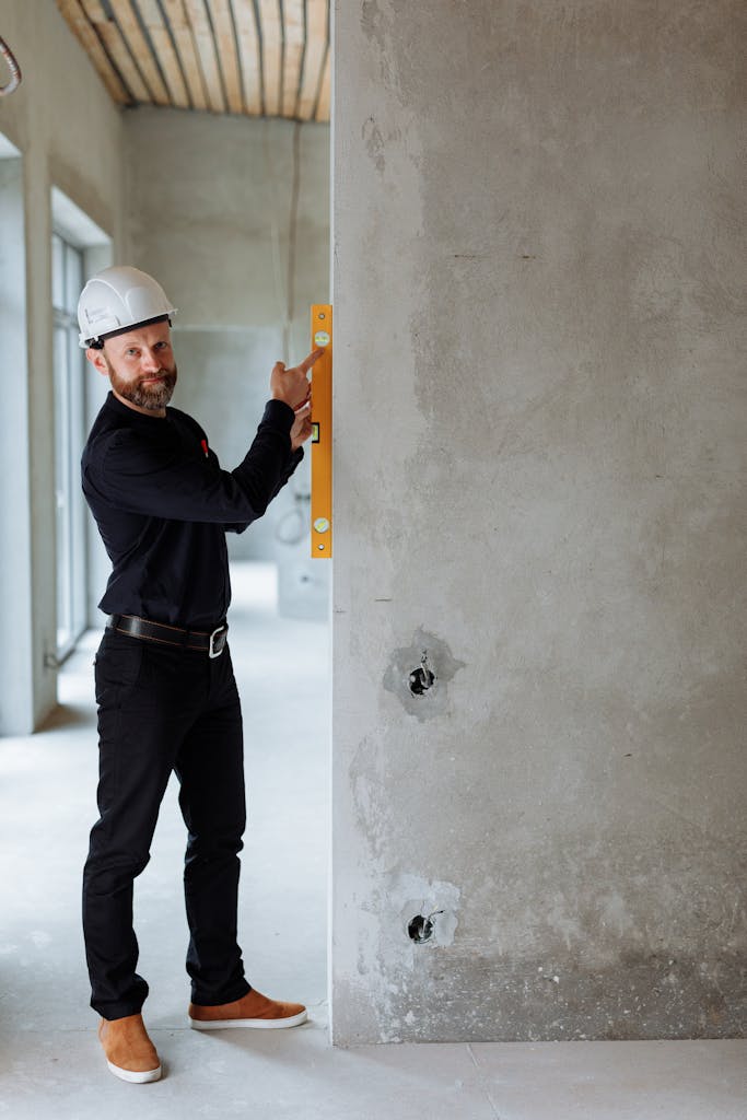 Smiling construction worker using spirit level on concrete wall at a building site.