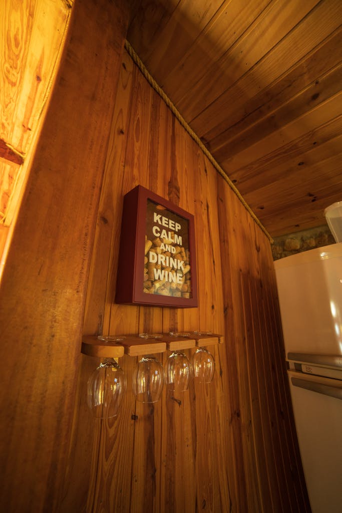 Decorative signboard with Keep Calm And Drink Wine inscription hanging on wall with set of wineglasses in kitchen near fridge in rustic house